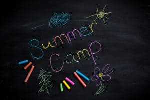 Text Summer camp written on black chalkboard, with chalk sticks of different colors