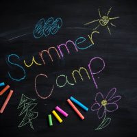 Text Summer camp written on black chalkboard, with chalk sticks of different colors